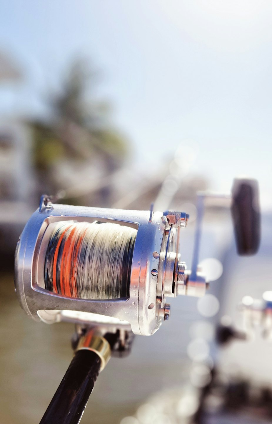 Shiny silver fishing reel with water droplets on a fishing rod.
